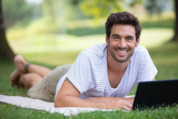 man lays on grass and uses a laptop