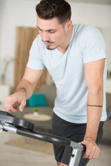 Plakat young adult man setting control panel of treadmill before running