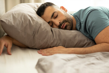 Portrait of peaceful european man sleeping in bed at home, lying with hand under pillow, resting...