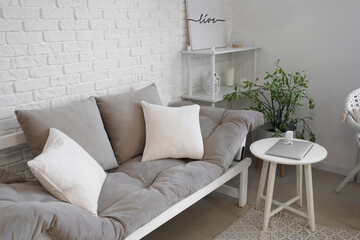 Cozy grey sofa with cushions and modern laptop on table in interior of living room