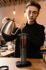 Barista is brewing aeropress coffee in cafe. Process of aeropress alternative method brewing coffee. Pouring hot water over roasted and ground coffee beans in aeropress.