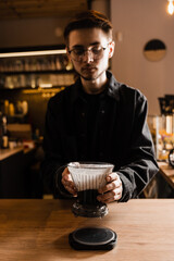 Barista holding pour over clever coffee dripper with ground coffee on paper filter before pouring water from drip kettle. Process of brewing pour over filter clever coffee dripper in cafe.