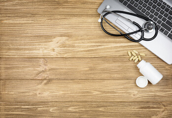 Stethoscope on laptop and bottle with pills on wooden table
