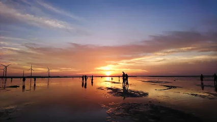 Foto op Plexiglas Gaomei Wetland, Taichung, Taiwan - August 11, 2018: sunset on wetland with windmills at the side, people silhouette in the front and reflection on the water © Claudia