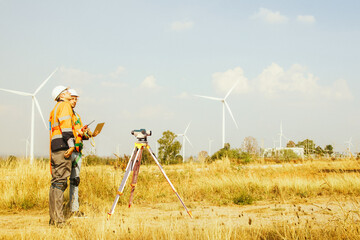 Fototapeta na wymiar Side view teamwork architect male surveyor team working with surveyor's telescope measure heights of walk in areas surveying wind generating fields to plan road construction with professional tools.