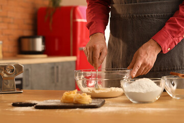 Man making dough for pasta at table in kitchen, closeup