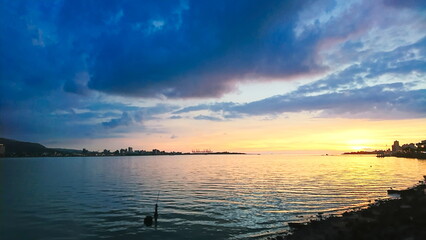 Naklejka premium Tamsui, Taipei, Taiwan - July 9, 2017: sunset at the ocean with a blue and cloudy sky and buildings in the background