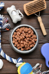 Composition with bowl of wet food and pet care accessories on wooden background