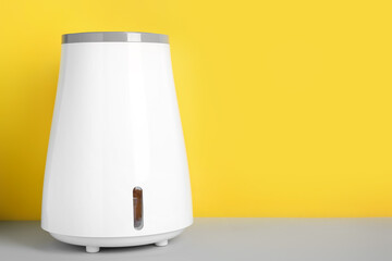 Modern humidifier on table near yellow wall