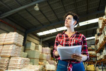 Woman inspecting warehouse to check quantity of goods on shelves. Woman examining storehouse.