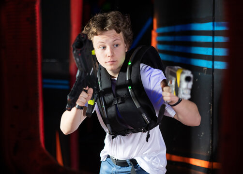 Portrait of positive young man with laser gun having fun with her friends on lasertag arena
