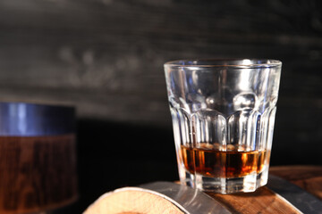 Glass of tasty whiskey on barrel against dark wooden background, closeup