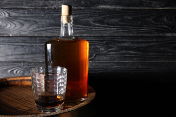 Glass and bottle of tasty whiskey on barrel against dark wooden background