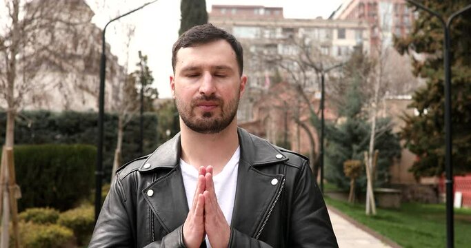 Man greeting with namaste gesture on street.