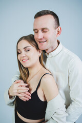 Fototapeta premium Beautiful young couple in love hugging on a white background. A stylish couple embraces and enjoys feelings. Men and women in stylish casual clothes