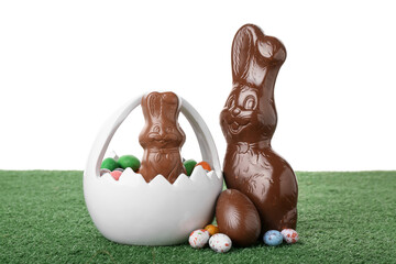 Chocolate Easter bunnies with eggs on green grass against white background
