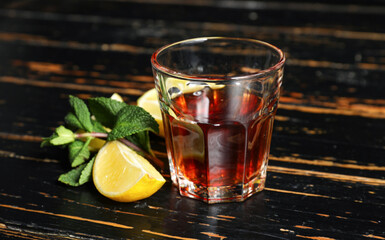 Glass of rum with lime and mint leaves on dark wooden background