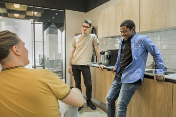 Fototapeta premium Group of cheerful young people talking and smiling during coffee break time in the office. Team of professional software developer relaxing in the canteen.