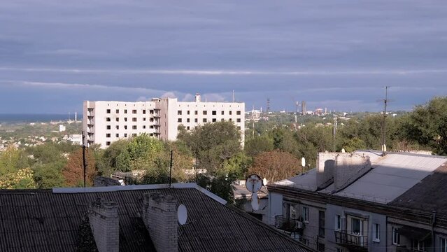 Moving Gray Cumulus Clouds on the Background of an Empty Abandoned Building. Gloomy view of old city. Factory. Shadow. Roofs of houses. Trees Swaying. Wind. Overcast. Horizon. Sunset. Bright sun rays.