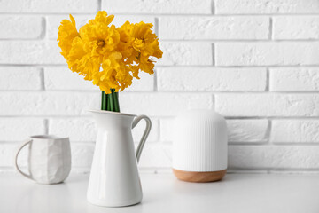 Vase with narcissus flowers and cup of tea on table near white brick wall