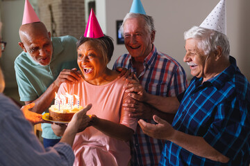 Happy group of diverse senior friends celebrating birthday with cake and presents