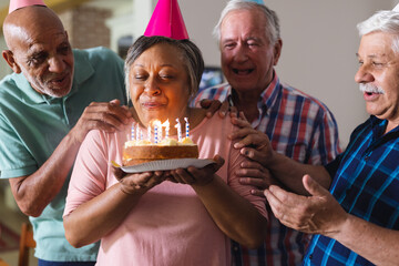 Happy group of diverse senior friends celebrating birthday with cake and presents