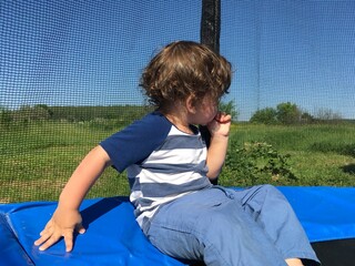 turning away looks at nature pensive cute curly child sits on a trampoline
