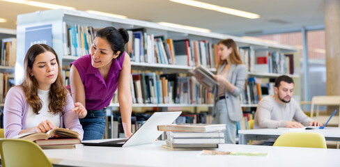 Caring woman helping friend to prepare for exams in public library