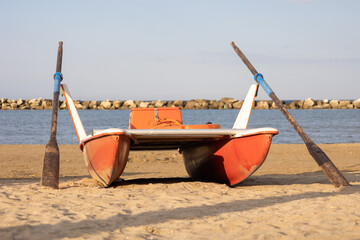 Classic italian rescue boat flanked by oars or rescue rowing catamaran on the sandy beach on the sunset symbolizing preparedness and safety along the tranquil shoreline.Vacation concept.