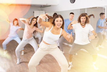 Fototapeta premium Active positive diverse men and women performing dance elements during lesson in modern fitness gym