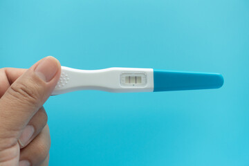 Young woman hand holding positive pregnancy test result with two stripes on pastel blue background. Closeup. Point of view shot. Top down view. Empty place for text.
