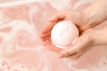 Woman with bath bomb above water, closeup