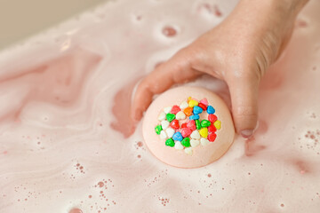 Woman putting bath bomb into water, closeup