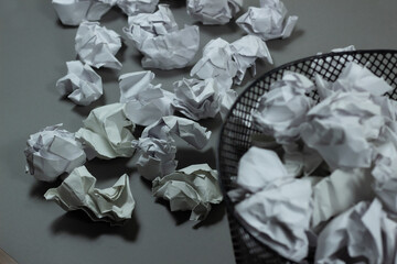 wastebasket overflowing with crumpled paper balls due to creative blockage