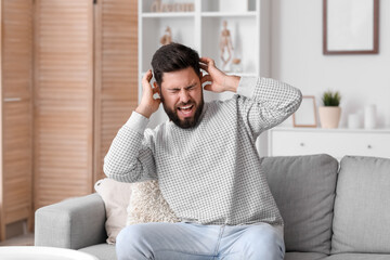 Angry young man suffering from loud noise at home - obrazy, fototapety, plakaty