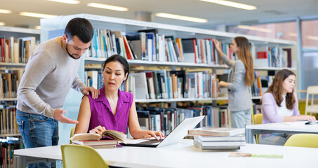 Man helping woman to prepare for exams in public library