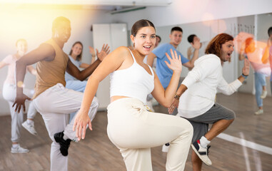 Excited multiethnic men and women exercising active moves with knee lifting in dance center indoors