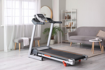 Interior of light room with modern treadmill and sofa