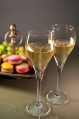 Glasses of sparkling white wine champagne or cava with bubbles and sweet dessert colorful macarons biscuits on background