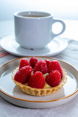 Breakfast with cup of black coffe and baked small tart with cream and fresh ripe red raspberry fruits