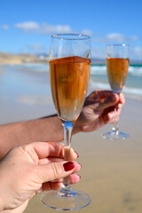 Beach party, hands with glass of rose champagne or cava sparkling wine, view on white sandy tropical beach and blue ocean water, romantic vacation, winter sun on Fuerteventura, Canary, Spain