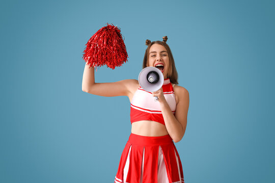 Beautiful cheerleader shouting into megaphone on blue background