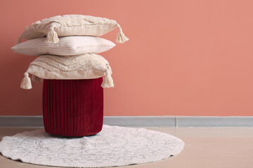 Stack of stylish decorative pillows on pouf near pink wall