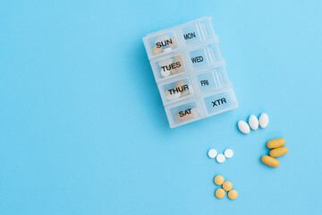 Top view of pill organizer with variety of pills and supplement. Weekly Pill container on blue background with copy space