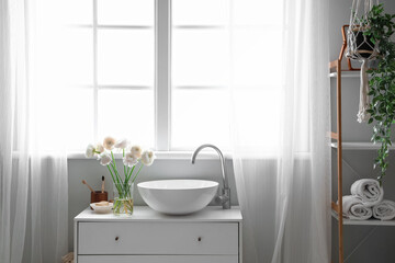 Fototapeta na wymiar Vase with ranunculus flowers and sink on chest of drawers in bathroom