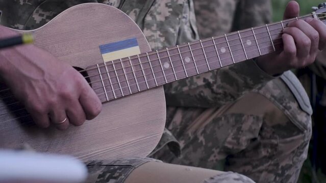 Ukrainian solider playing guitar near bonfire on battlefield