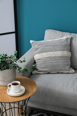 Fototapeta na wymiar Grey sofa with cushion and cup of coffee on table near blue wall