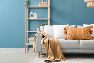 Grey sofa with cushions and plaid near blue wall