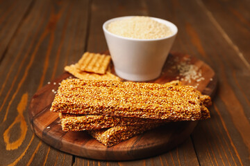 Board with tasty kozinaki and sesame seeds on wooden background