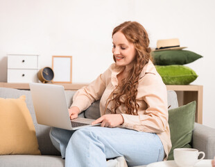 Beautiful redhead woman using laptop on sofa at home